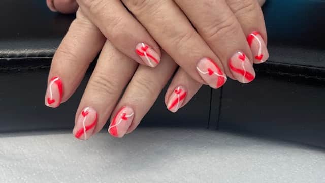Hands with beautifully manicured nails featuring red and white heart designs, resting on a black surface.