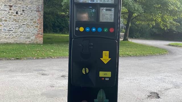 Parking machine with payment options, surrounded by greenery and a stone wall in Clapham, Yorkshire Dales National Park.