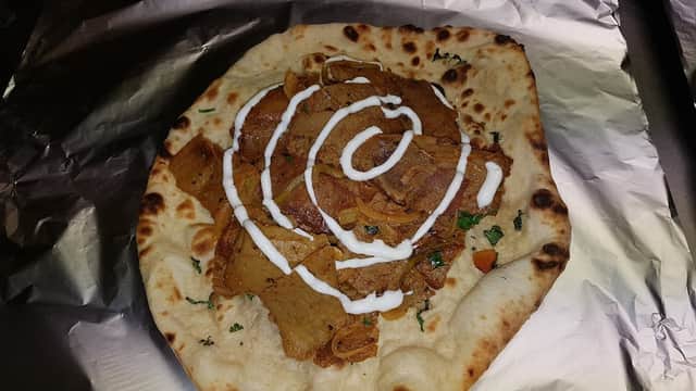 A naan topped with spiced meat, drizzled with yogurt sauce and garnished with herbs, served on foil.