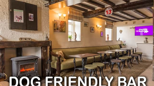 Cozy interior of The Angel Inn with a fireplace, seating, and a TV displaying Absolute Radio, featuring a dog-friendly sign.