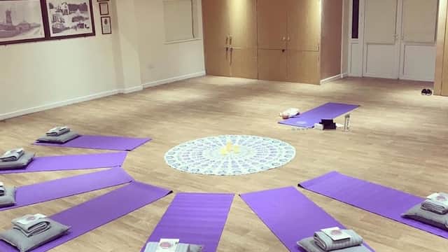 Yoga mats arranged in a circular pattern around a central mandala on a wooden floor in a spacious room.