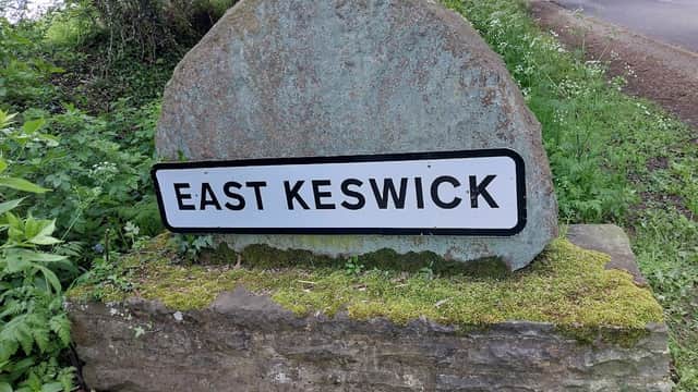 Stone sign reading "EAST KESWICK" surrounded by greenery near a road in Bardsey, Yorkshire.