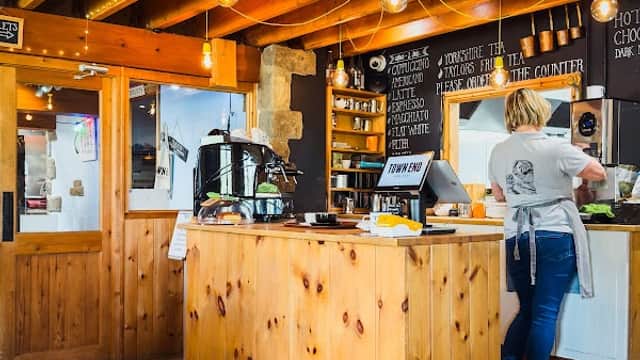 Wooden counter with menu board, warm lighting, and a staff member preparing food in a cozy shop atmosphere.