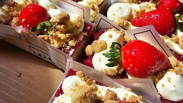 Delicious layered desserts topped with strawberries, cream, and crumbles, arranged neatly in small containers.
