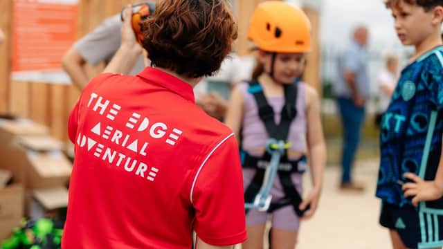 A staff member in a red shirt assists children in harnesses, preparing for an aerial adventure at The Edge in Yorkshire.