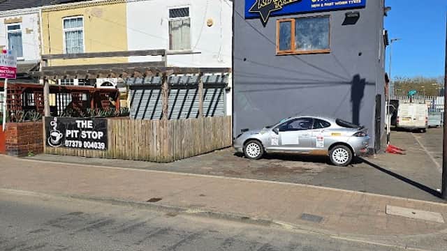 Kinsley Tyres garage with a grey building, parked car, and sign displaying contact information under a clear blue sky.