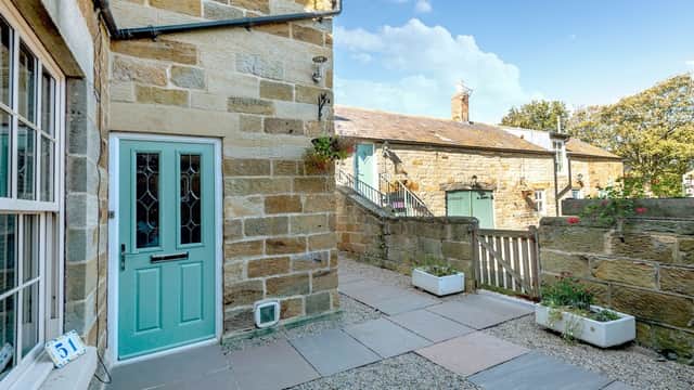 Charming stone cottage entrance with a teal door, pathway, and lush greenery in Port Mulgrave, Yorkshire.