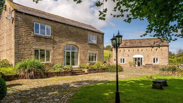 Two stone cottages with large windows, surrounded by greenery and a cobblestone path, in a scenic Yorkshire setting.