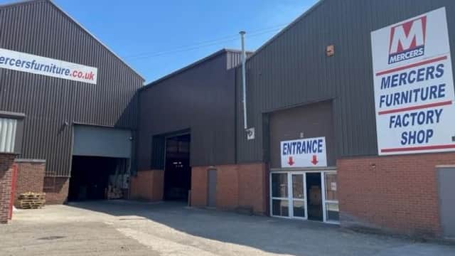 Mercers Furniture Ltd factory shop entrance with large signage, brick facade, and industrial buildings under a blue sky.