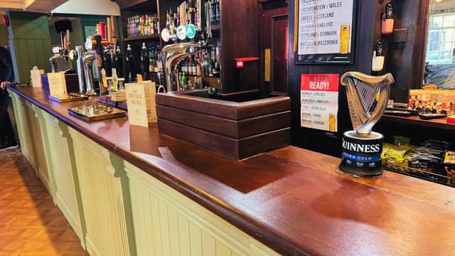 Wooden bar with taps, drinks, and a Guinness can; match day promotions displayed on a sign.