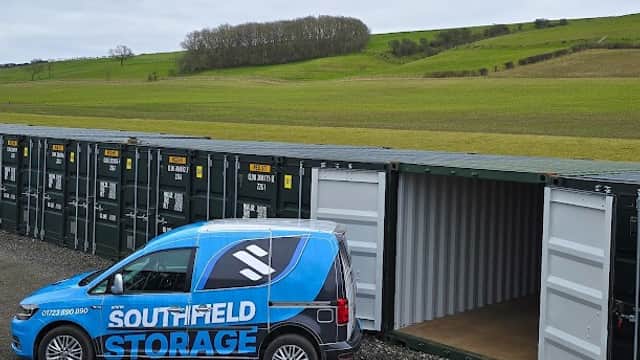 Southfield Storage van parked beside storage containers with green hills in the background under a cloudy sky.