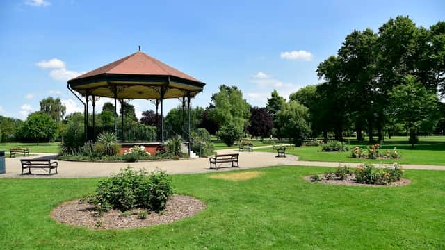 Victorian-style bandstand surrounded by well-maintained gardens and benches in a sunny park setting.