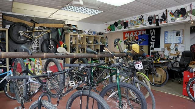 Bikes displayed on racks with shelves of cycling gear and tools in a shop interior.