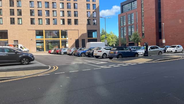 Pay & Display car park with various parked cars, surrounded by modern buildings and a clear blue sky.