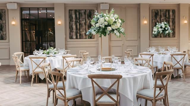 Elegant dining setup with round tables, white tablecloths, and tall floral centerpieces in a stylish venue.