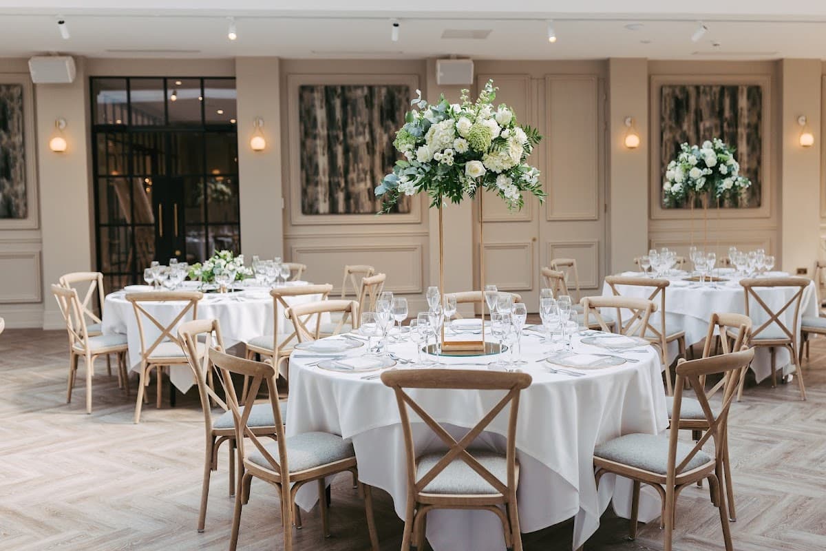 Elegant dining setup with round tables, white tablecloths, and tall floral centerpieces in a stylish venue.