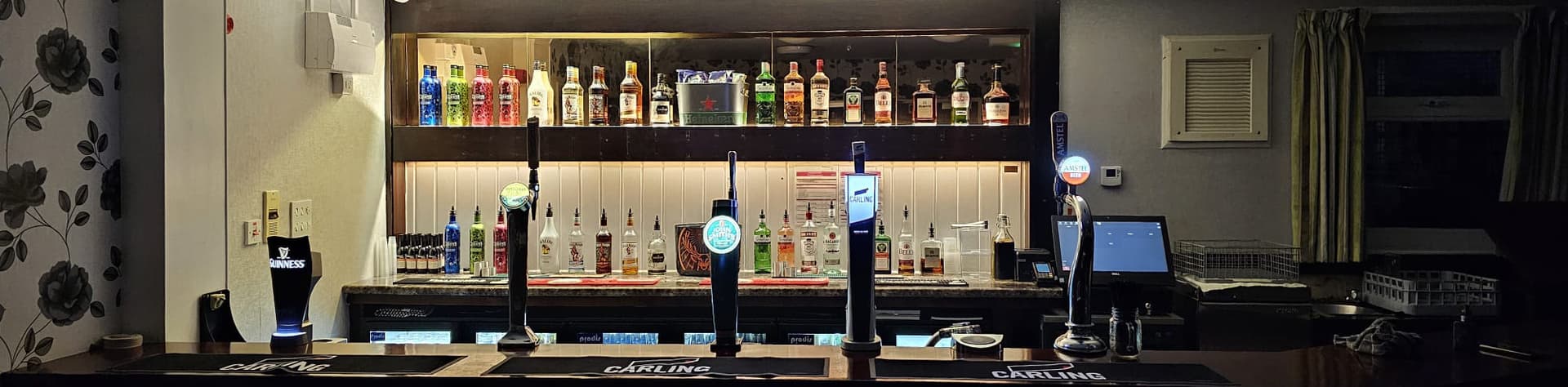 Bar area with illuminated beer taps, shelves of liquor bottles, and a stylish counter in a cozy venue setting.