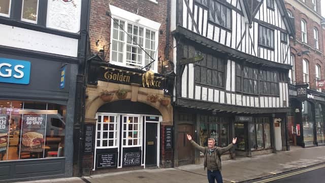 Historic pub with timber-framed architecture, signage for "Golden Fleece," and a person standing with arms outstretched.
