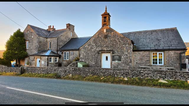 Stone building with a slate roof, bell tower, and surrounding dry stone wall, set against a scenic rural backdrop.