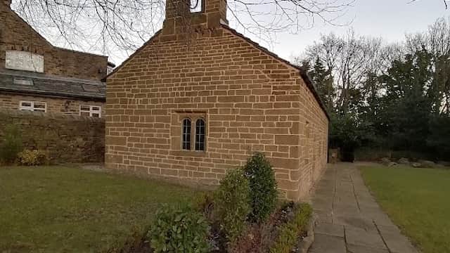 Stone building with a bell tower, surrounded by greenery and a stone pathway, set in a tranquil outdoor area.