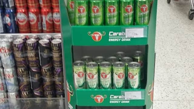 Display stand for Caraboo energy drinks, featuring vibrant green cans and a sign promoting the orange flavor.