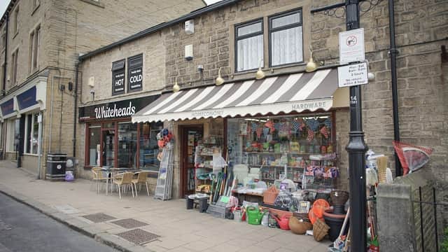 Ironmongers storefront with striped awning, colorful gardening supplies, and outdoor seating in Farsley, Yorkshire.
