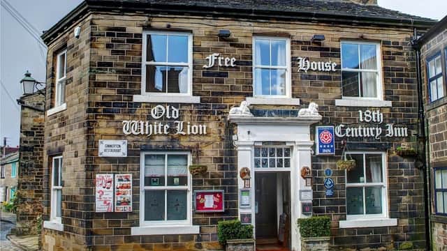 Historic stone building with a sign reading "Old White Lion," featuring a welcoming entrance and decorative plants.
