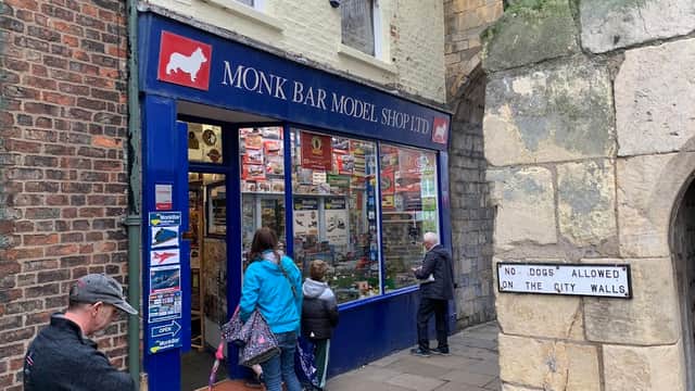 Colorful storefront of Monk Bar Model Shop with people browsing, surrounded by historic stone walls.