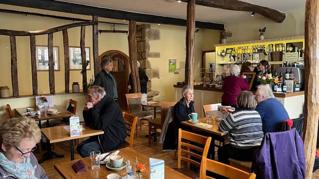 Cozy café interior with wooden beams, patrons enjoying coffee, and a barista serving at the counter.