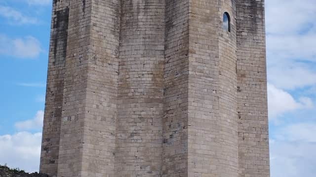 Conisbrough Castle's stone tower with a flag, set against a blue sky and grassy landscape.