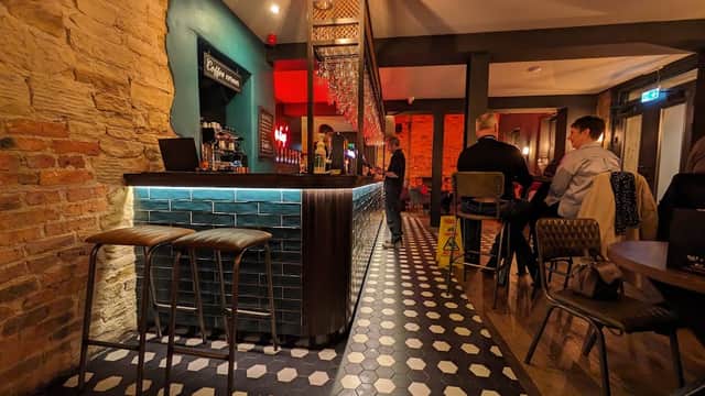 Stylish bar interior with a blue-tiled counter, wooden stools, and patrons enjoying drinks in a cozy atmosphere.