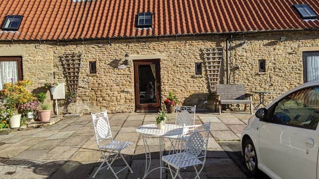 Charming stone cottage with a red-tiled roof, outdoor seating area, and flower pots in a picturesque courtyard.