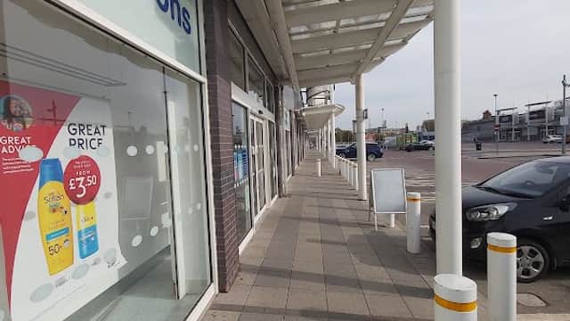 Sidewalk view of Kingston Retail Park with shops, a clear sky, and parked cars.