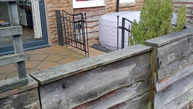 Rustic stone cottage with a slate roof, surrounded by a wooden fence and a small garden area.