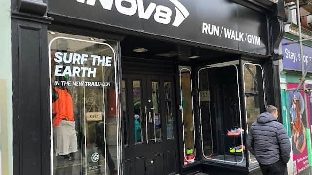 INOV8 store front featuring running shoes, colorful displays, and a customer outside in a gray jacket.