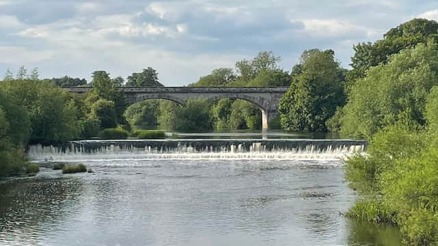 A serene river scene with a stone bridge and lush greenery lining the banks, under a cloudy sky.