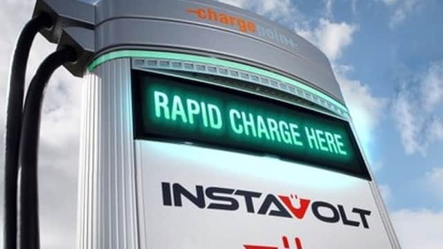 InstaVolt charging station with illuminated sign reading "RAPID CHARGE HERE" against a cloudy sky.