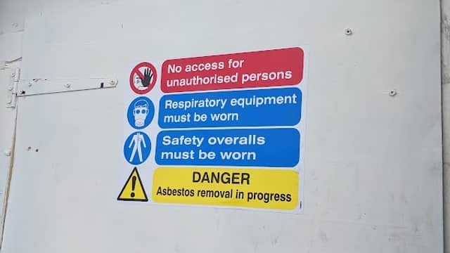 Signage indicating safety precautions for asbestos removal, including warnings and required protective gear.