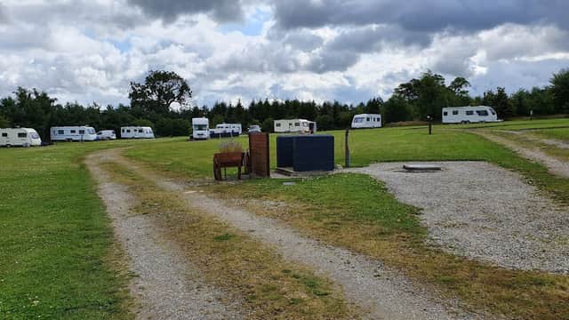 Caravan park with grassy areas, gravel paths, and several parked caravans under a cloudy sky.