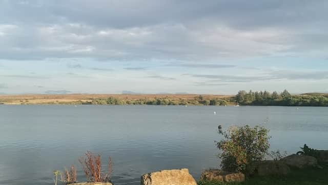 Calm water of Scaling Reservoir surrounded by greenery and rocky outcrops under a partly cloudy sky.