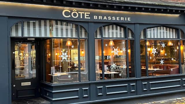Côte Brasserie restaurant exterior with large windows, warm lighting, and decorative snowflake designs.
