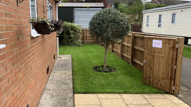 Brick exterior of Swaleside Cottage with a small garden, a tree, and a wooden fence with an open gate.
