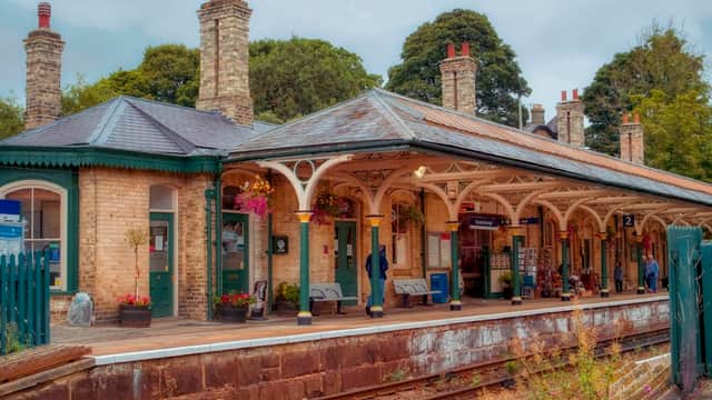 Victorian-style railway station with brick buildings, covered platforms, and potted flowers, surrounded by trees.