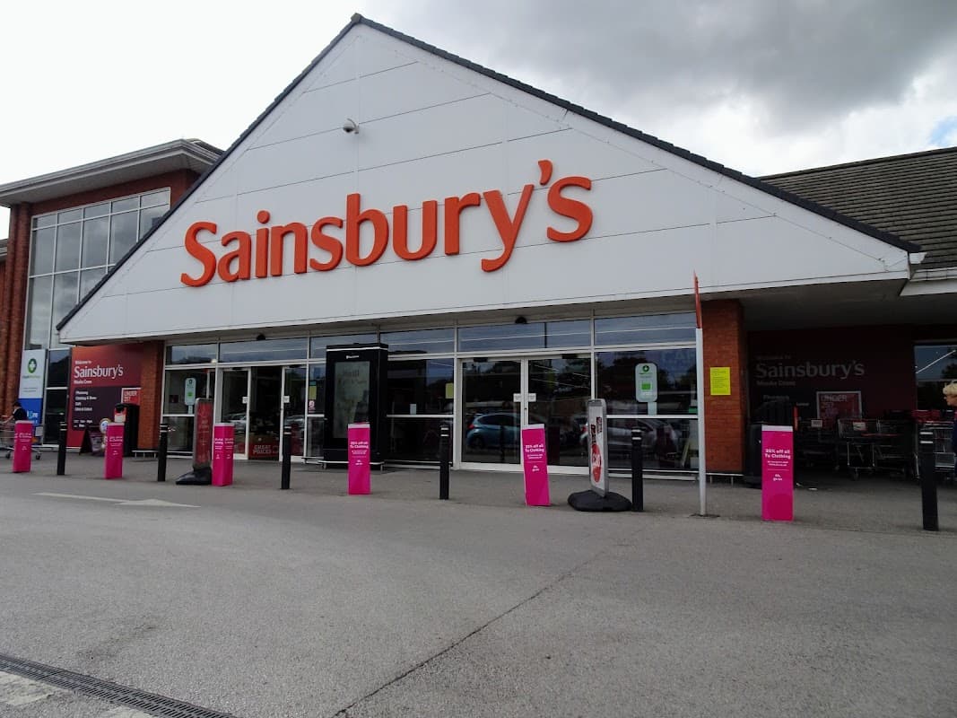 Sainsbury's storefront in Otley, Yorkshire, featuring large orange signage and pink promotional stands outside.