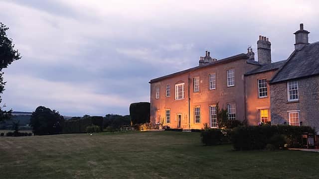 Langton Hall features a stone exterior with warm lighting, surrounded by a manicured lawn and trees under a cloudy sky.
