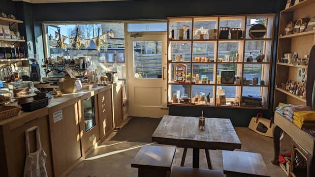 Bright shop interior featuring wooden shelves filled with products, a counter with coffee equipment, and a rustic table.