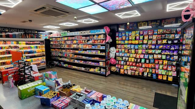 Colorful shelves filled with snacks, drinks, and sweets in a well-lit corner shop, with a vibrant ceiling design.