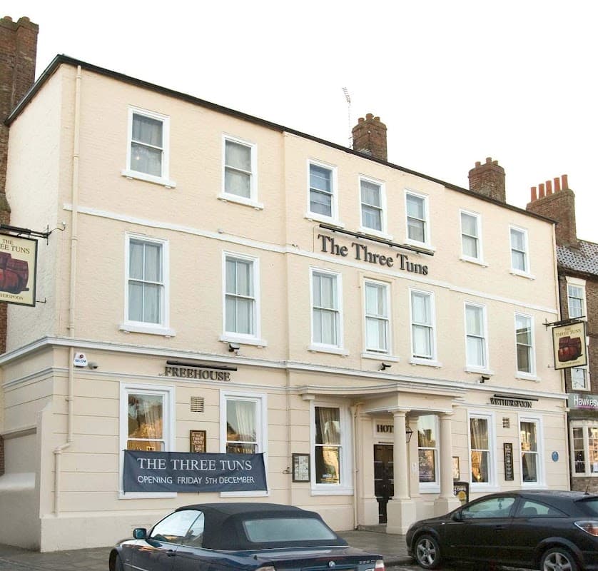 The Three Tuns restaurant with a cream-colored facade, large windows, and a sign announcing its opening date.