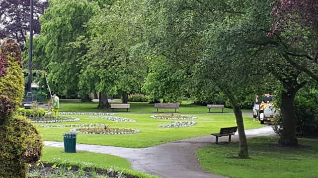 Lush green park with flower beds, benches, and a maintenance vehicle on a pathway under overcast skies.