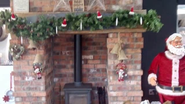 Cozy brick fireplace adorned with garlands, stars, and holiday decorations, featuring a Santa figure nearby.